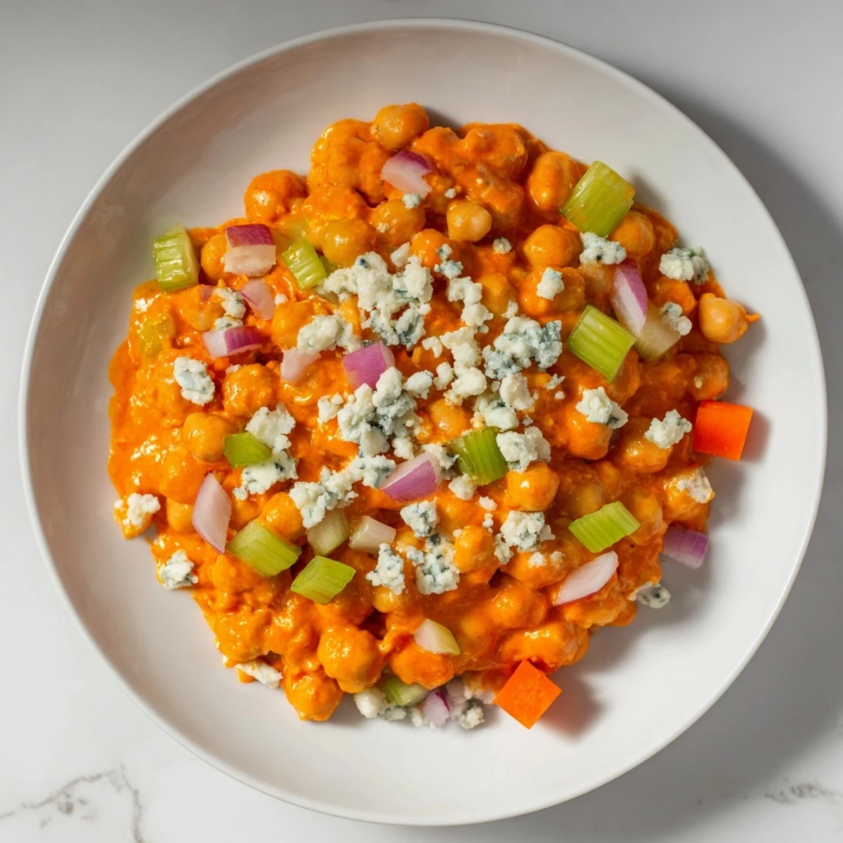 Spicy buffalo chicken bean salad tossed with vibrant carrots, celery, and a tangy buffalo sauce, ready to serve.