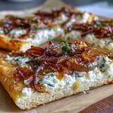 Auf einer Flammkuchenbasis liegt cremiger Ziegenkäse, bedeckt mit süßen karamellisierten Zwiebeln und einem Honig-Tropfen mit Chilinote.