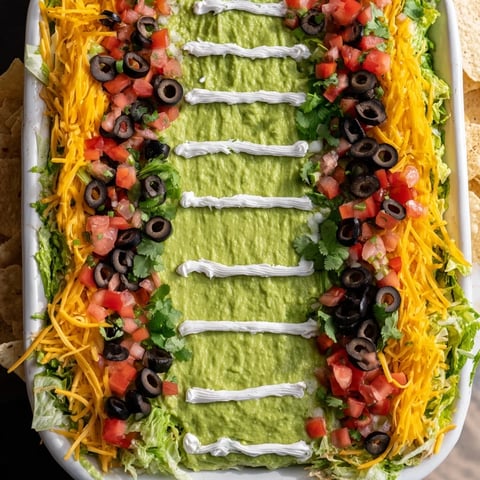 Vibrant Football Field Dip Platter, layered with cheeses, salsa, and creamy guacamole for game day snacks.