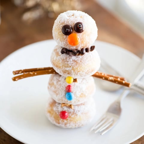 Mini Donut Snowman Stack ready to be assembled, featuring powdered sugar donuts and orange candy noses.