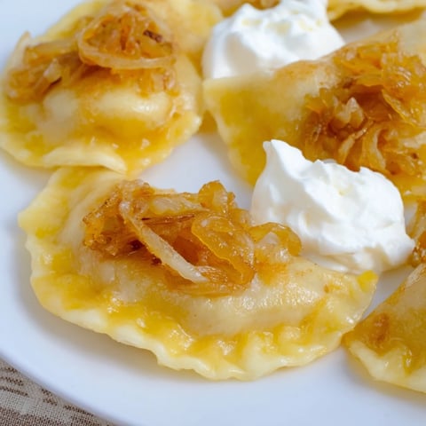 Golden, crispy Polish pierogi dumplings topped with sweet caramelized onions and a dollop of sour cream.