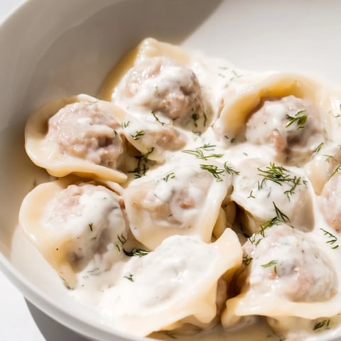 Golden Russian pelmeni, swimming in a rich sour cream sauce, ready to be enjoyed.