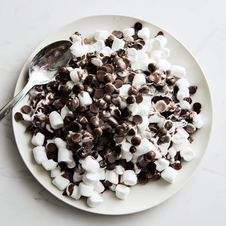 Ein Teller voller klebriger, geschmolzener Schokoladenstückchen und Marshmallows, ein schneller süßer, einfacher Genuss.