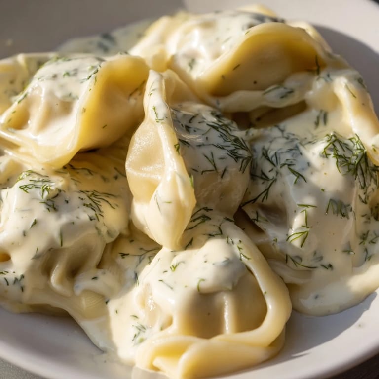 Steaming plate of homemade Russian pelmeni, with tender dumplings and creamy topping.