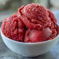 Strawberry-Daiquiri-Sorbet mit Limettenabrieb in einem Glas, mit frischen Erdbeeren und Minzblättern garniert.